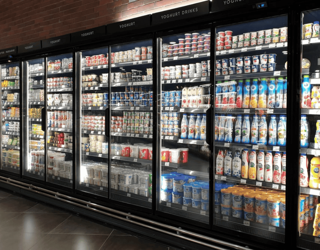 Glass-front refrigerated display cases stocked with dairy and frozen products in a Southern New England supermarket.