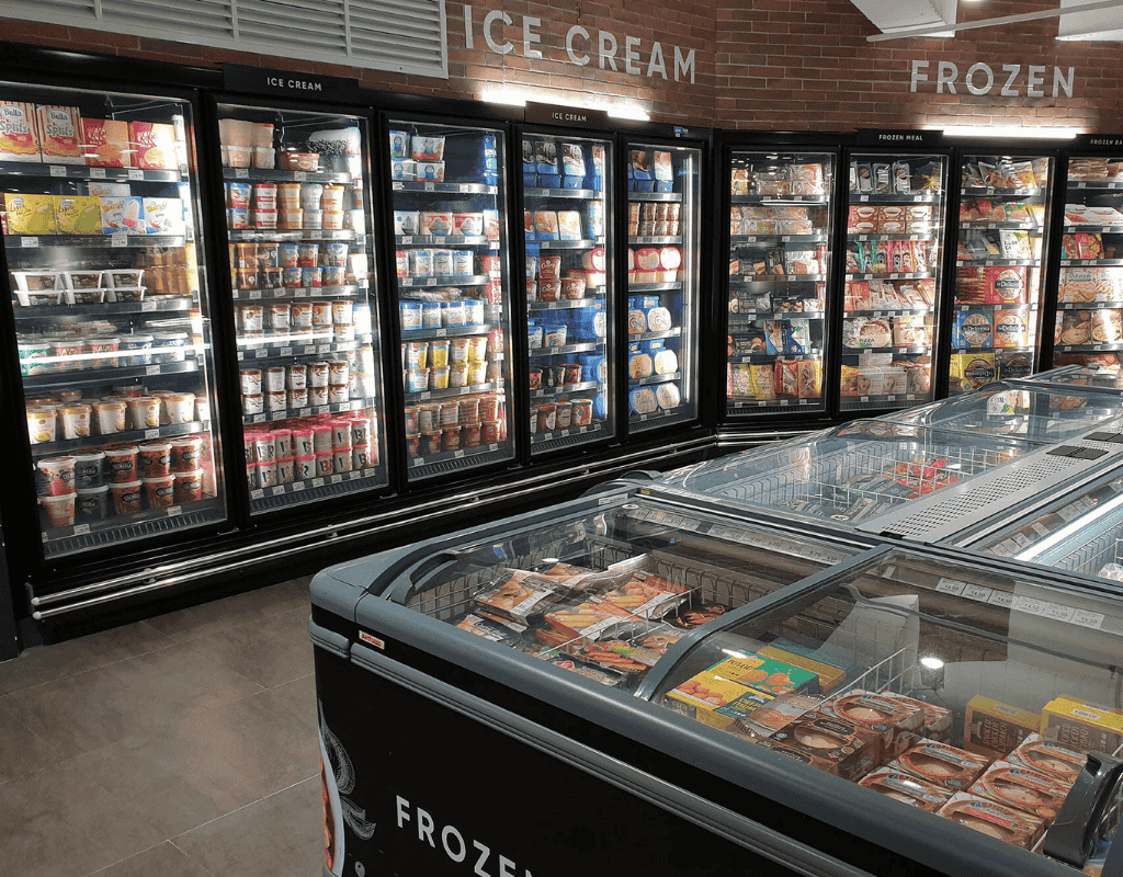 Glass-door retail refrigeration cases stocked with ice cream and frozen foods in a Southern New England grocery store.